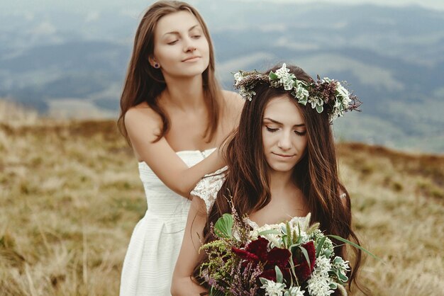 Stylish bridesmaid helping gorgeous bride preparing boho wedding luxury ceremony at mountains