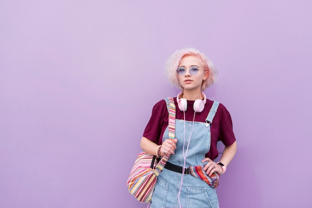 stylish bright young girl with headphones sunglasses and colored hair on a purple background