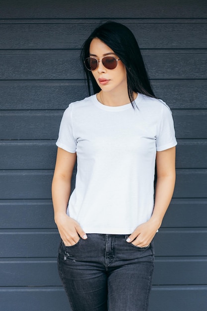 Stylish brunette asian girl wearing white tshirt and glasses posing against street urban clothing