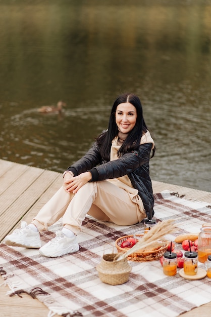 Stylish brunette girl in a leather jacket beige pants and white sneakers on the lake
