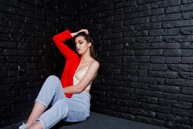 Stylish brunette girl on red jacket against studio black brick wall