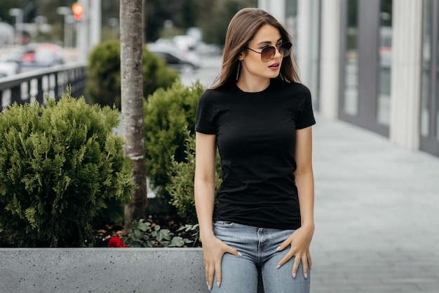 Stylish brunette girl wearing black tshirt and glasses posing against street  urban clothing style