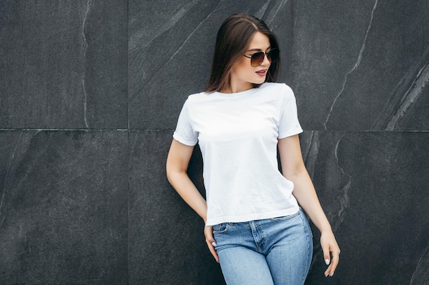 Stylish brunette girl wearing white tshirt and glasses posing against street  urban clothing style