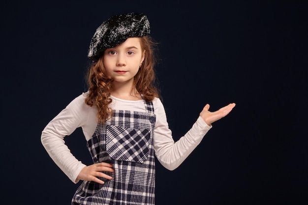 Stylish brunette kid is posing in studio on a black background. Children's fashion.