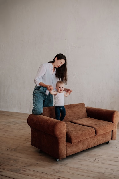 Stylish brunette mom plays with her little daughter on a brown sofa