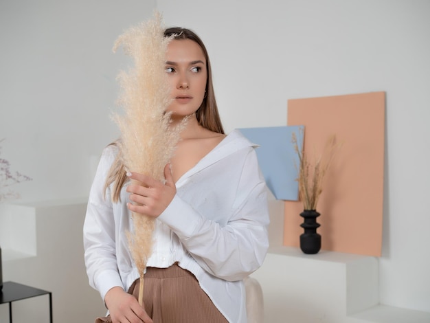 Stylish brunette in a white shirt with an armful of dry grass portrait in light colors