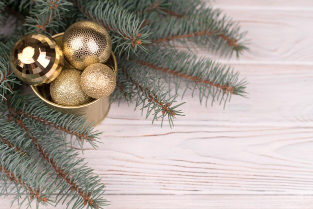 白い木製の背景とクリスマスツリーの枝にクリスマスの黄金のおもちゃのスタイリッシュなバケツ