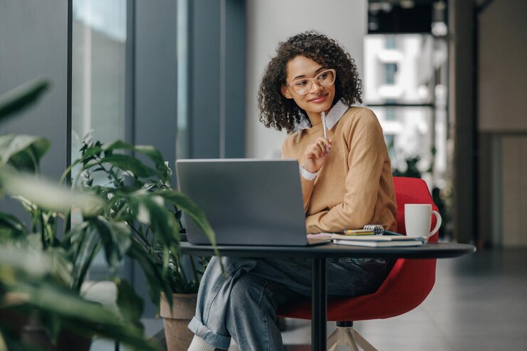 Photo stylish business woman in eyeglasses working on laptop while sitting in modern office near window