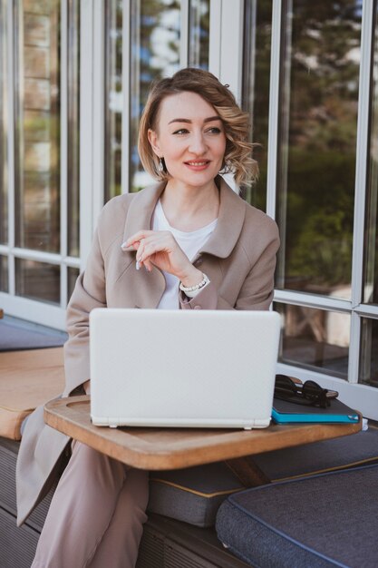 Stylish business woman in a street cafe working on laptop