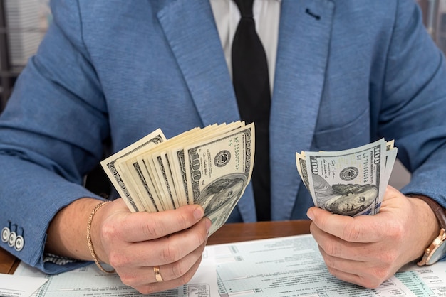 Stylish businessman counts a large sum of dollars and fills out tax forms 1040 in his office