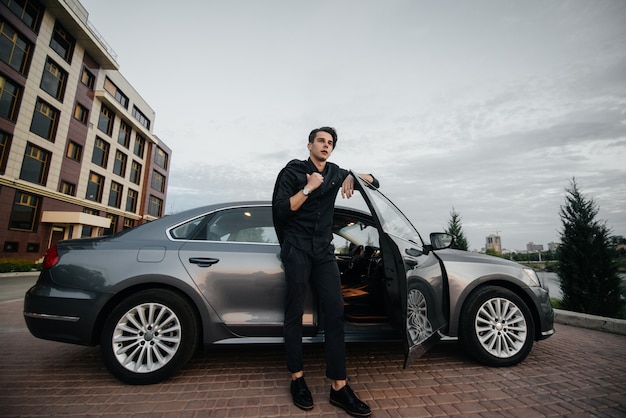 A stylish businessman smokes cigars near a luxury car. Fashion and business