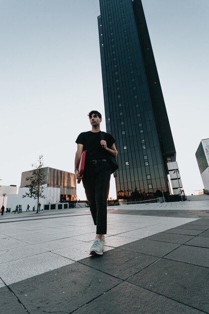 Stylish businessman student on the way to office during a colourful sunset. Business, education,lifestyle concept.Serious model with tshirt.Copy space.Big building scenery, banking and administration.