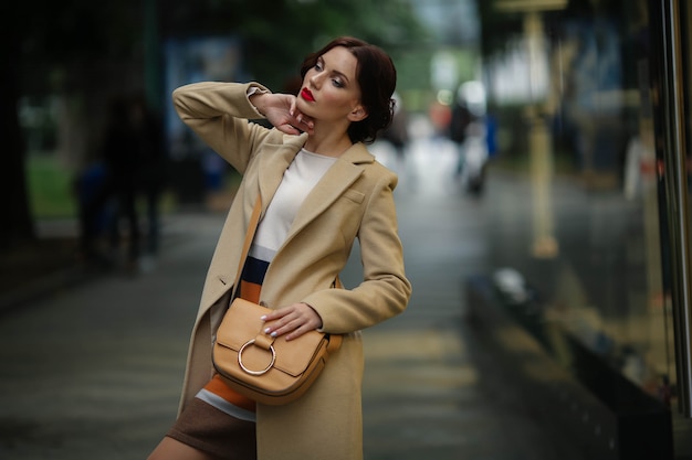 Stylish businesswoman 25 years old in a white coat on a background of a street with shops