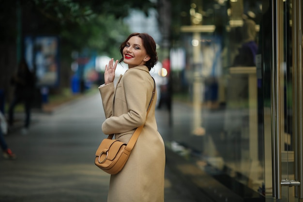 stylish businesswoman 25 years old in a white coat on a background of a street with shops