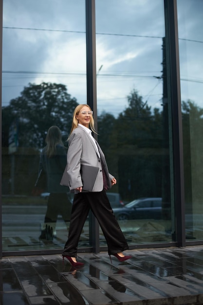 Stylish businesswoman holding laptop looking at camera walking on the street Successful