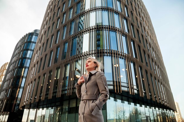 Stylish businesswoman in open air against business center. Woman in gray coat in business district