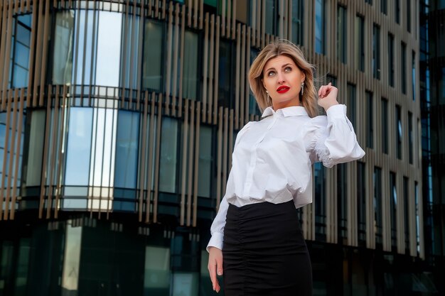 Stylish businesswoman in open air against business center. Woman in white blouse in business district