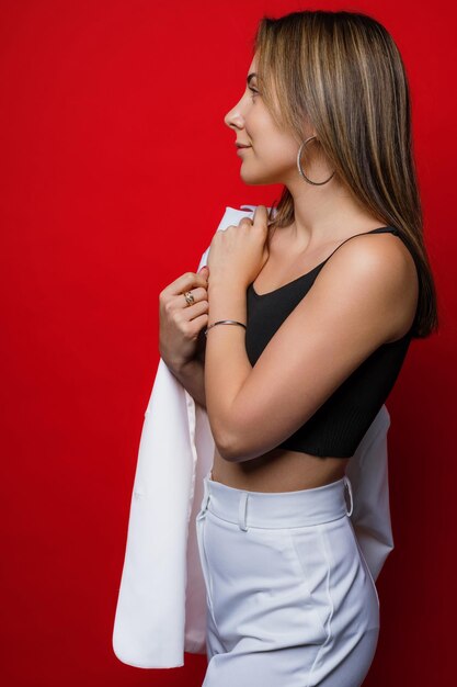 A stylish businesswoman with a white suit poses in the studio Model on a red background in the studio