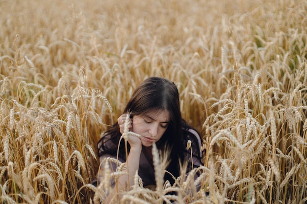 Stylish calm woman sitting in wheat field in evening light Summer countryside Rural slow life