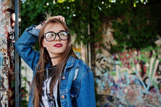 Stylish casual hipster girl in jeans wear and glasses against large graffiti wall