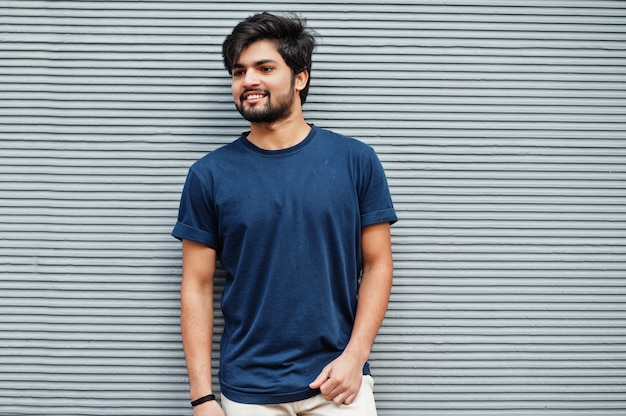 Stylish casual indian man wear blue t-shirt posing against grey wall.