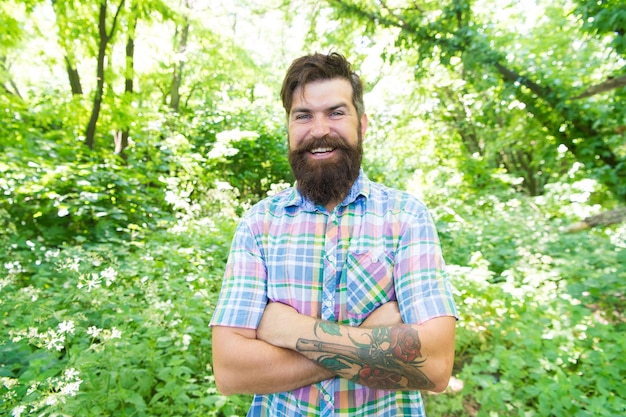 Stylish and casual Stylish hipster keeping arms crossed on summer outdoor Bearded man with stylish hair wearing casual shirt on sunny day Happy fashion model smiling with stylish look