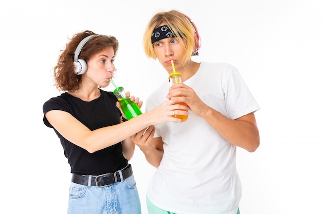 Stylish caucasian blonde man and young woman drinks juice and listen to music isolated on white wall