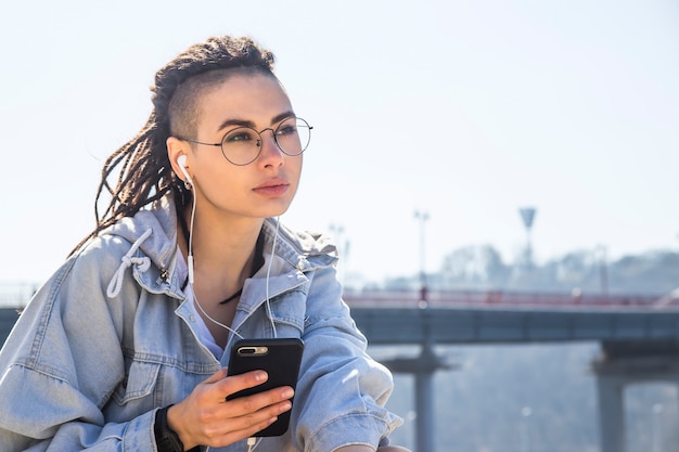 Ragazza caucasica alla moda che ascolta la musica con le cuffie e che riposa in natura in primavera