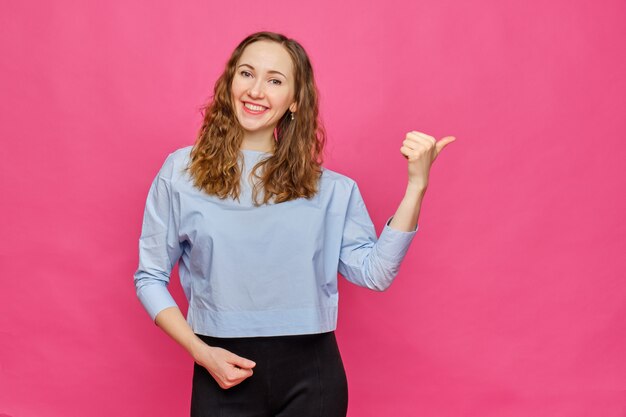 Stylish caucasian girl in a pale blue t-shirt pointing finger to abstract object on a pink background.