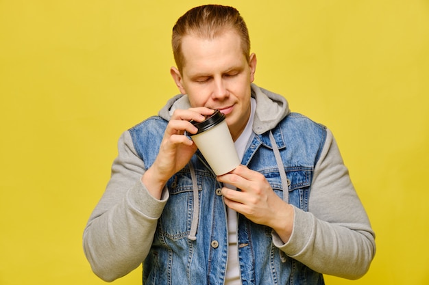 Stylish Caucasian man in jeans holding a disposable paper cup for coffee