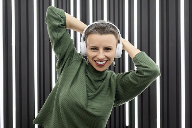 Stylish caucasian woman in headphones with a wide smile on the background of a backlit wall