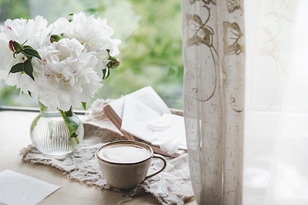 写真 窓にカーテンとガラスの花瓶でコーヒーと泡を入れたスタイリッシュなセラミックカップ 居心地の良い家