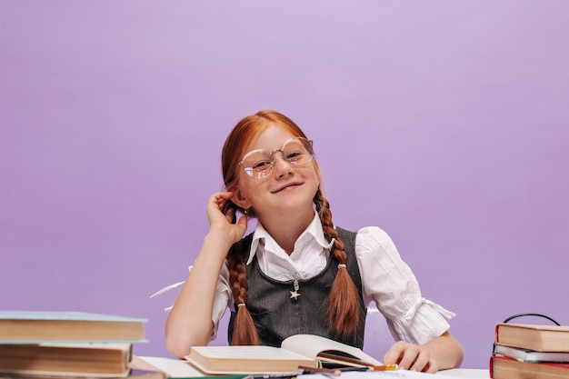 Stylish charming young girl with ginger pigtails in cool round eyeglasses and stylish school outfit looking into camera