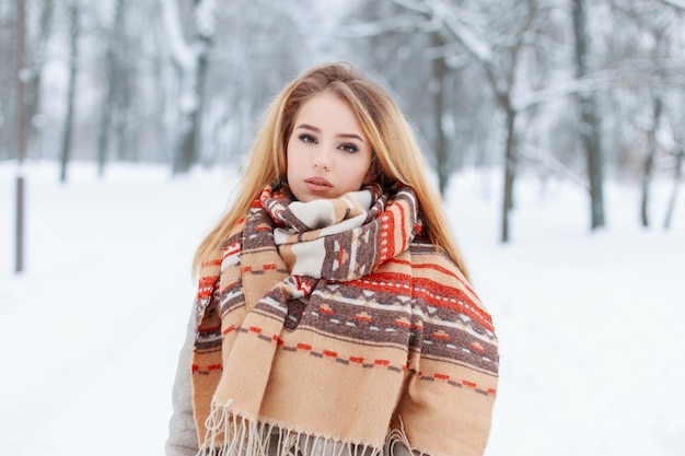 Стильная очаровательная молодая женщина-блондинка в винтажном шерстяном шарфе с красивым рисунком в сером пальто