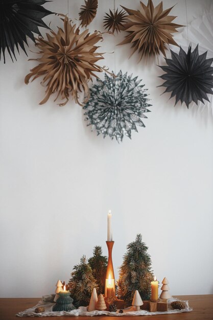 Stylish christmas candles and trees decorations on wooden table
and big paper stars merry christmas