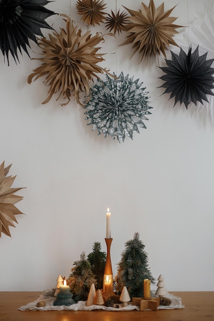 Stylish christmas candles and trees decorations on wooden table\
and big paper stars merry christmas