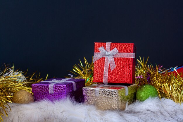Стильная новогодняя открытка с красочными подарочными коробками, елочными шарами и праздничной мишурой. Скопируйте пространство сверху на темном фоне.