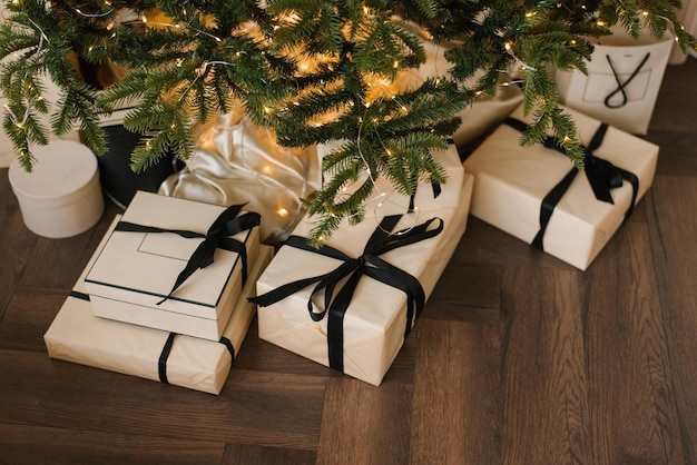 Стильные рождественские подарки лежат под елкой с огнями сверху