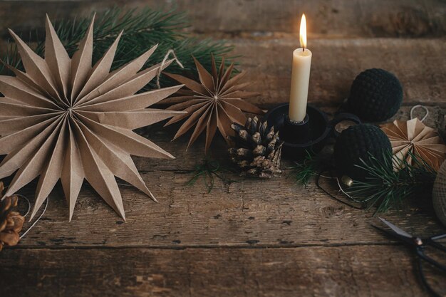 Stylish christmas paper stars candle ornaments pine cone on\
rustic wooden background xmas advent