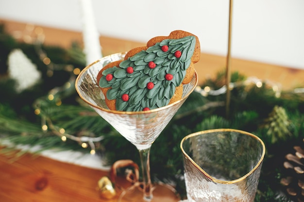 Stylish christmas table setting christmas tree cookie in
wineglass plate with linen napkin vintage cutlery fir branches with
golden lights candles on table holiday dinner creative table
set