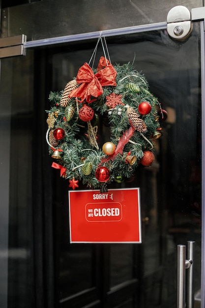 Stylish christmas wreath red bow and baubles and Sorry we closed sign on doors of building Modern christmas decor in city street Winter holidays in Europe Merry Christmas