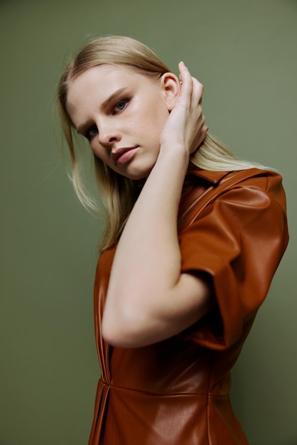 Stylish closeup portrait for banner design Sexy blonde female in leather brown palette clothes looks over her shoulder at camera posing isolated on over green studio background