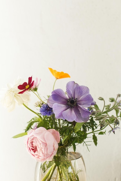 Stylish colorful flowers bouquet on rustic wall background Beautiful summer wildflowers anemones and roses in vase gathered from garden floral arrangement in modern room in home