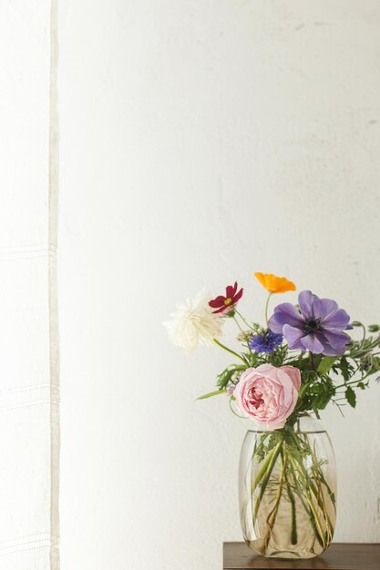 Stylish colorful flowers bouquet on rustic wall background Beautiful summer wildflowers anemones and roses in vase gathered from garden floral arrangement in modern room in home