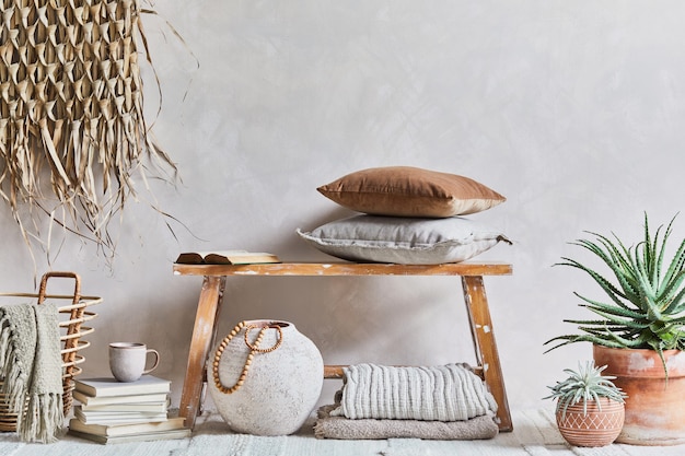 Stylish composition of cozy living room interior with copy space, bench in retro style, clay vase, crockery, straw wall decoration and textiles. Rustic inspiration. Summer vibes. Beige wall. Template.