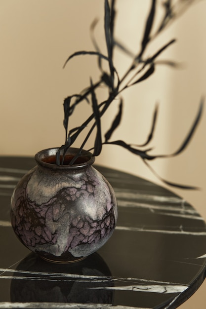 Stylish composition at fancy interior with marble coffee table, dried black flower in vase in modern home decor. Details. Template.