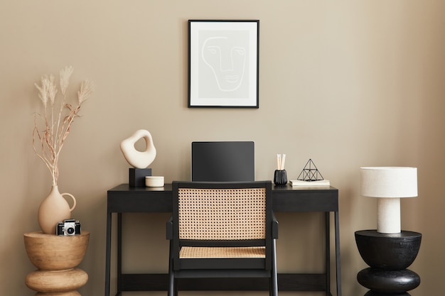 Elegante composizione di interni per l'home office con scrivania in legno nero, sedia, fiori secchi in vaso, laptop, cornice per poster mock up, tazza di caffè, orologio ed eleganti accessori per ufficio. modello.