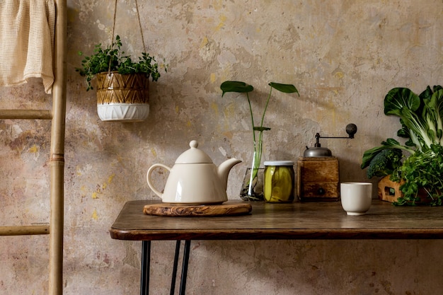 Stylish composition of kitchen interior with family table, vegetables, tea pot, dessert, food supplies, plants and kitchen accessories in wabi sabi concept of home decor.