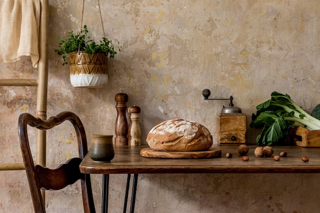 Stylish composition of kitchen interior with family table, vegetables, tea pot, dessert, food supplies, plants and kitchen accessories in wabi sabi concept of home decor.