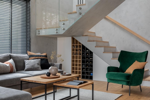 Elegante composizione dell'interno del soggiorno con divano ad angolo grigio velluto verde poltrona tavolino in legno pavimento in legno mobili di design e accessori personali modello di arredamento per la casa moderno